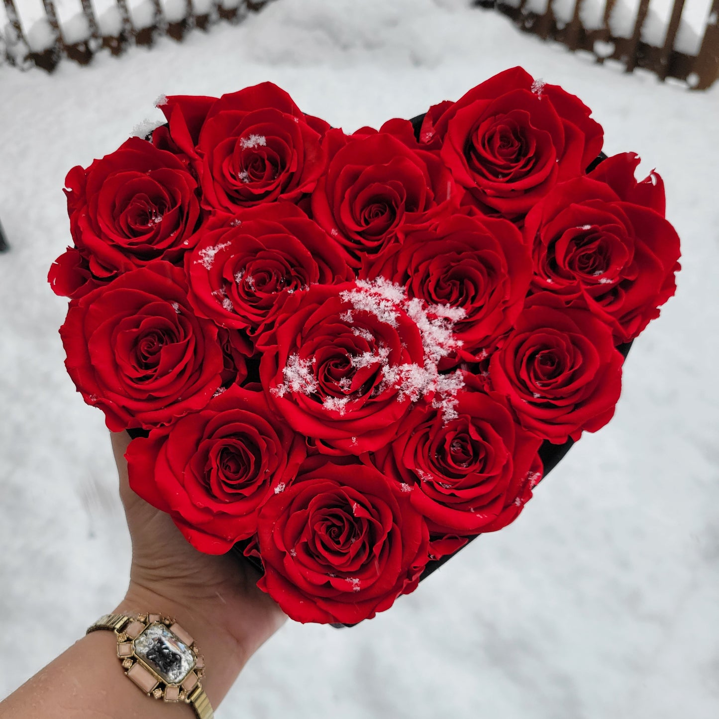 Heart-shaped arrangement of red roses held by a person with a blurred snowy background